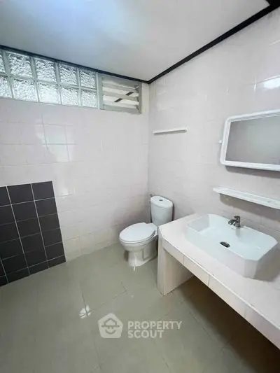 Spacious bathroom with modern fixtures and tiled walls, featuring a sleek sink and toilet.