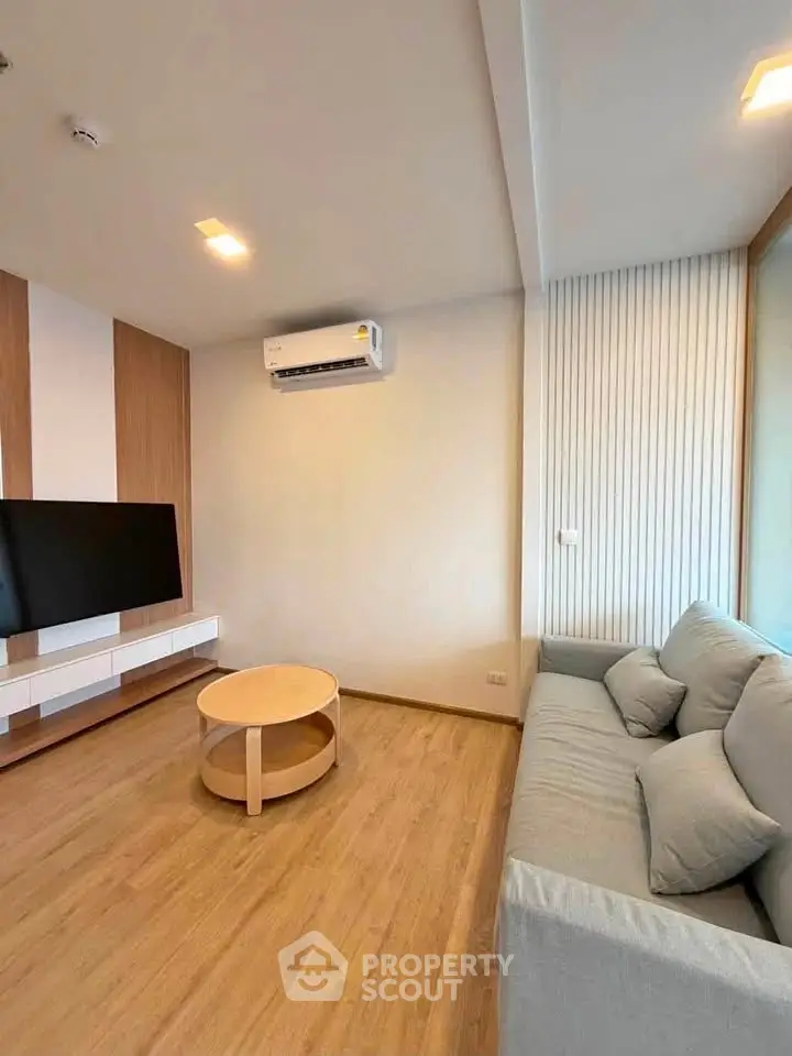 Modern living room with sleek design, featuring a wall-mounted TV, air conditioning, and comfortable sofa.