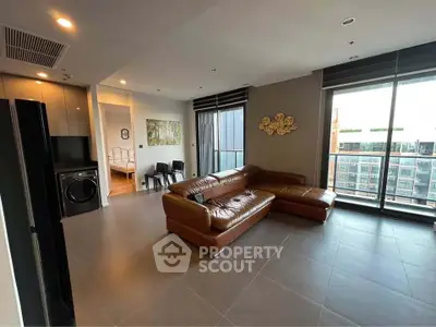 Spacious modern living room with leather sectional and large windows offering city views.