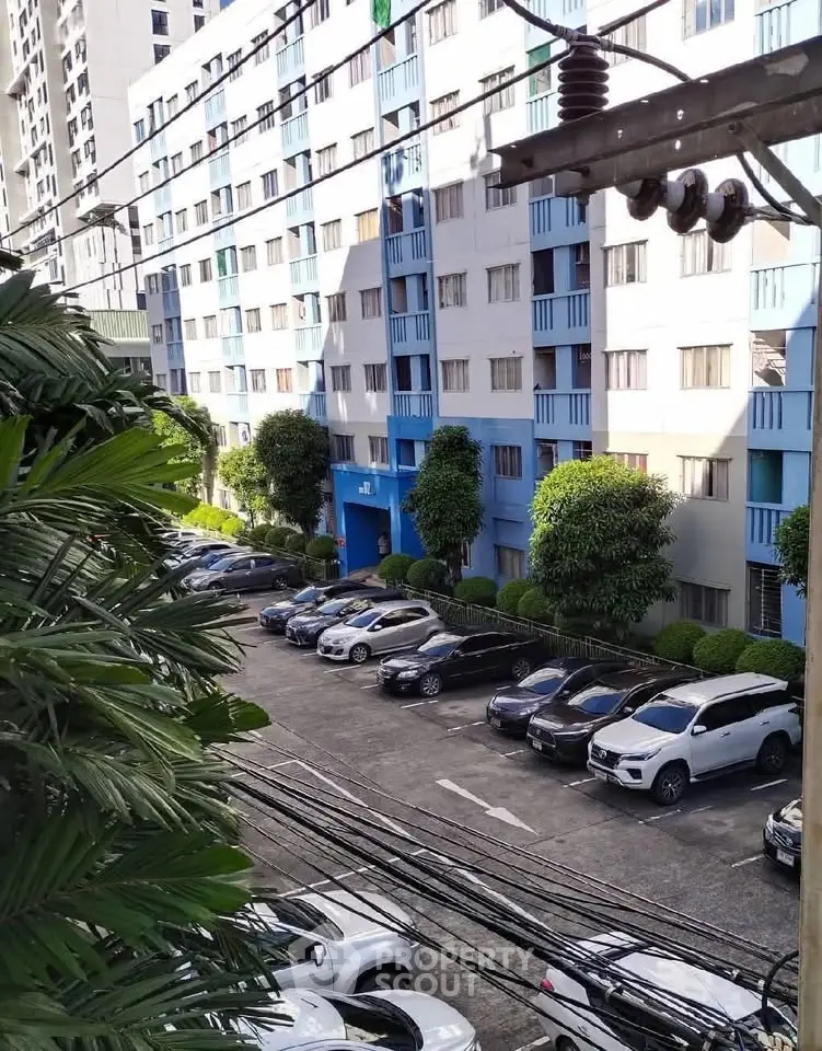 Modern apartment building with parking area and lush greenery, offering urban living convenience.