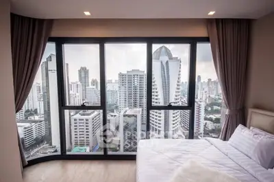 Luxurious bedroom with stunning city skyline view from large windows.