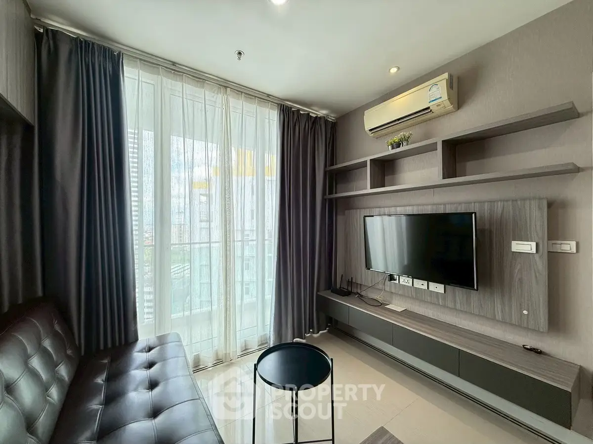 Modern living room with sleek furniture and large window offering city views.