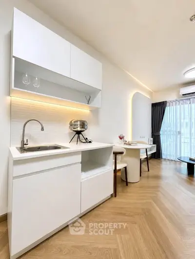 Modern open-layout kitchen with sleek white cabinets and cozy dining area, featuring elegant lighting and wooden flooring.