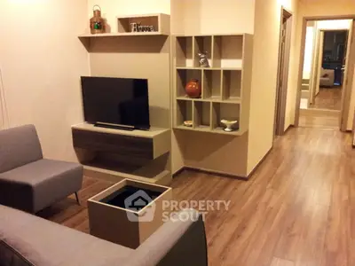 Modern living room with sleek furniture and wooden flooring, featuring a flat-screen TV and stylish shelving.