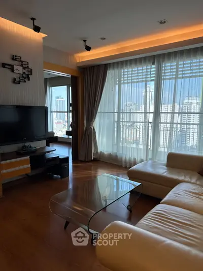 Spacious living room with modern decor and city view, featuring a glass coffee table and leather sofa.