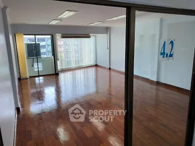 Spacious empty room with polished wooden floors and large windows offering natural light.