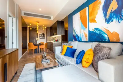 Modern living room with vibrant decor and open kitchen layout, featuring stylish furniture and colorful artwork.