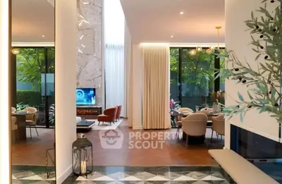 Luxurious modern living room with elegant dining area and floor-to-ceiling windows overlooking lush greenery.
