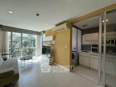 Modern living room with open kitchen and large windows offering natural light and garden view.