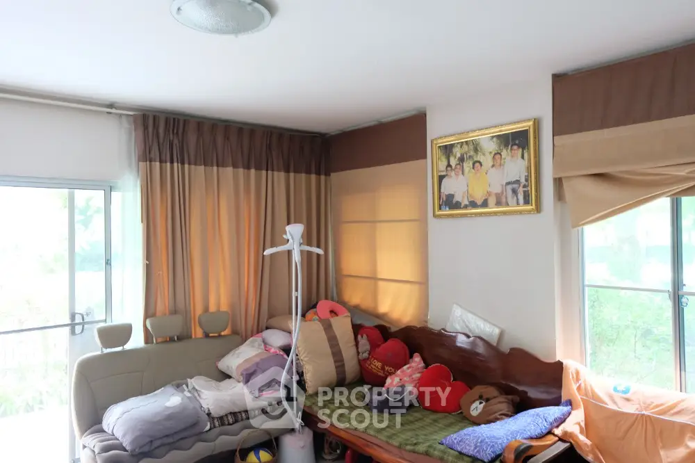 Cozy living room with natural light, featuring a comfortable sofa and large windows with curtains.