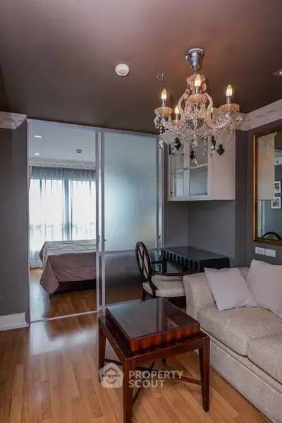 Elegant living room with chandelier and sliding doors leading to a cozy bedroom
