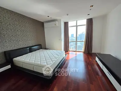 Spacious bedroom with city view, featuring elegant hardwood floors and modern furnishings.