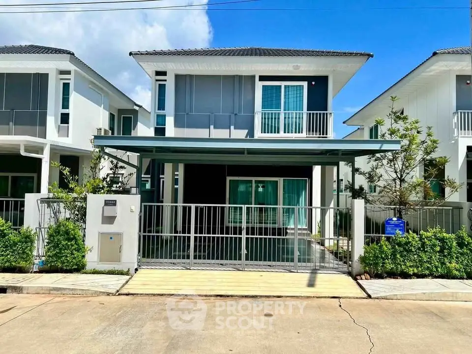 Modern two-story house with balcony and gated driveway in sunny neighborhood.