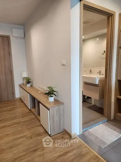 Modern apartment hallway with wooden flooring leading to a stylish bathroom.