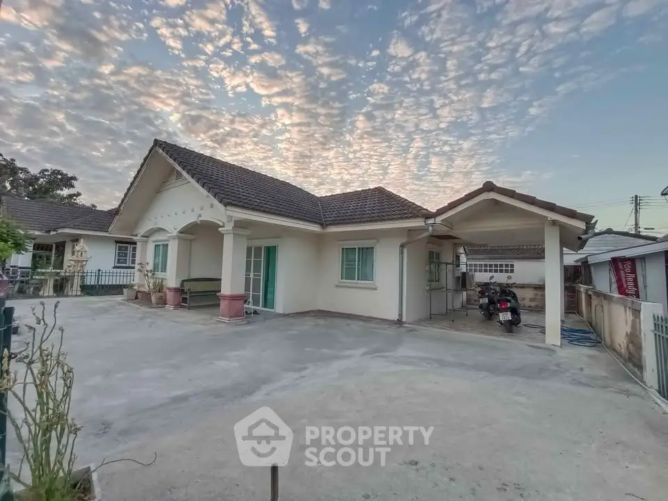 Charming single-story home with spacious driveway and carport under a picturesque sky.