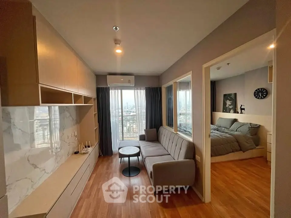 Modern apartment with open living room and bedroom, featuring wooden floors and large windows with city views.