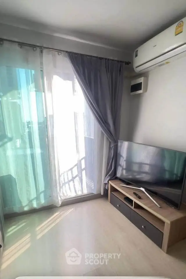 Bright living room with modern TV setup and air conditioning, featuring floor-to-ceiling windows and elegant curtains.