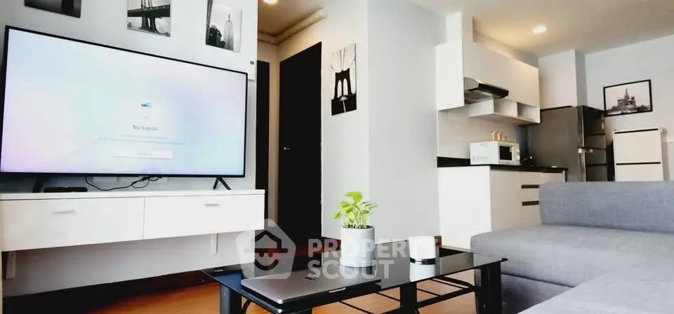 Modern living room with sleek furniture and open kitchen layout, featuring a large TV and stylish decor.