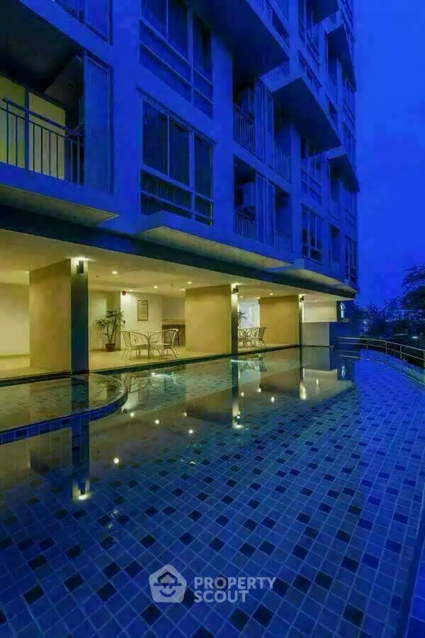 Luxurious apartment building with illuminated poolside area at dusk, showcasing modern architecture and serene ambiance.