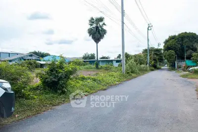 Scenic suburban road with lush greenery and distant houses, ideal for peaceful living.