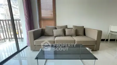 Modern living room with beige sofa and glass coffee table, featuring floor-to-ceiling windows and city view.