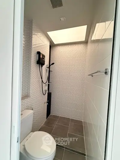 Modern bathroom with sleek shower and skylight, featuring hexagonal tiles and contemporary fixtures.