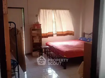 Cozy bedroom with natural light, featuring a bed, bookshelf, and window with curtains.