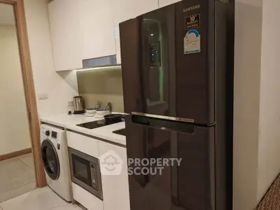 Modern kitchen with sleek appliances including fridge, washing machine, and microwave in compact layout.