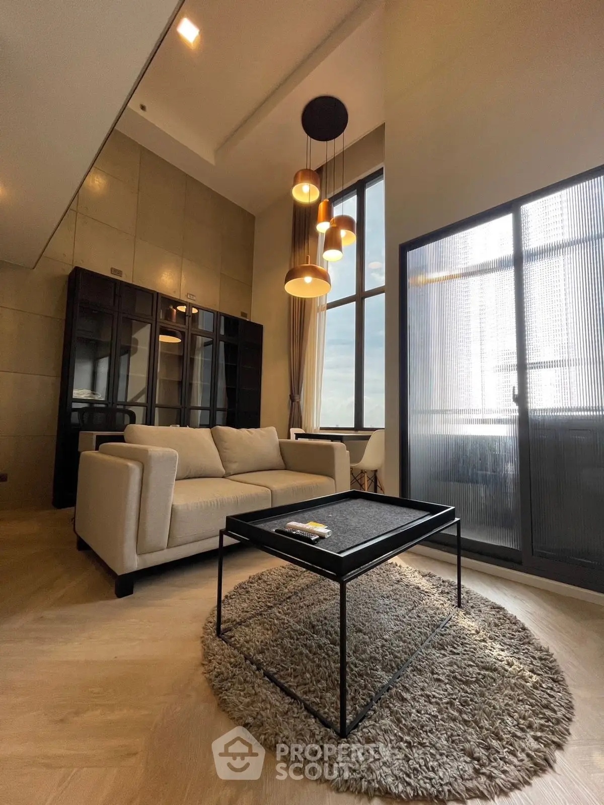 Modern living room with high ceiling, elegant lighting, and large windows offering natural light.