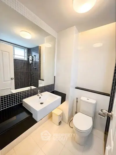 Modern bathroom with sleek black and white tiles, featuring a large mirror and contemporary fixtures.