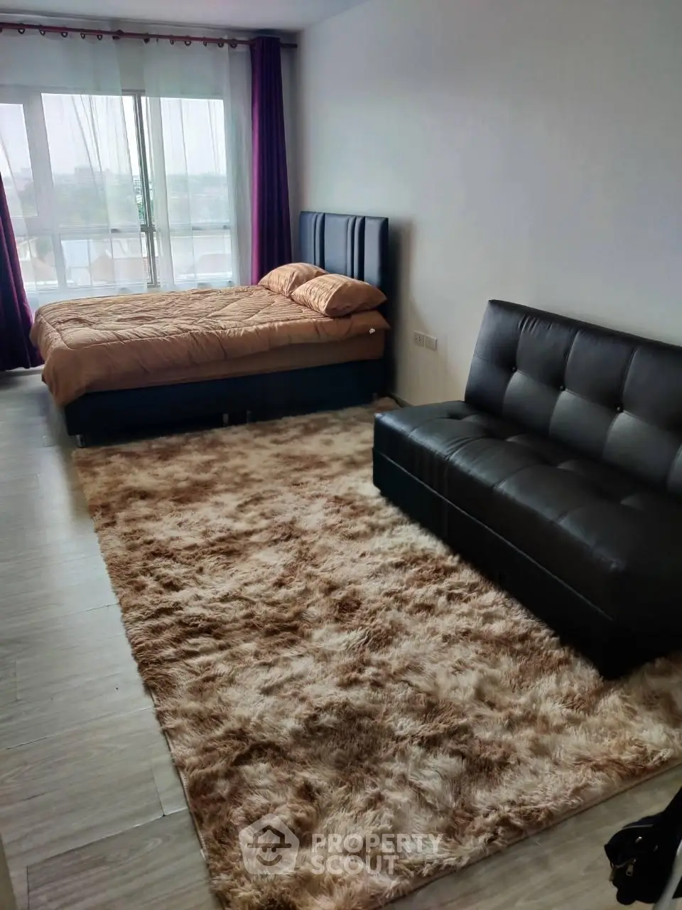 Modern studio apartment with cozy bed and stylish sofa, featuring large windows and plush carpet.