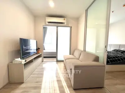 Modern living room with sleek sofa and TV, adjacent to a cozy bedroom through sliding glass doors.