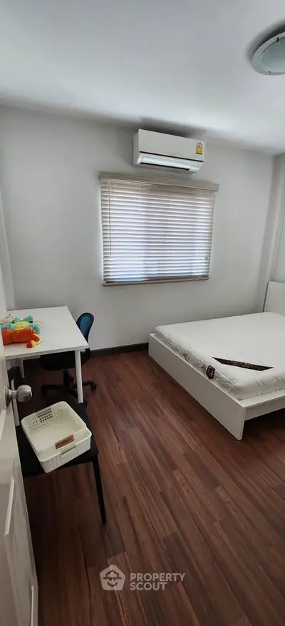 Cozy bedroom with wooden flooring, featuring a bed, desk, and air conditioning for comfortable living.