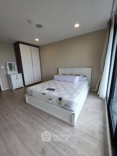 Spacious bedroom with large window and modern furnishings in a stylish apartment.