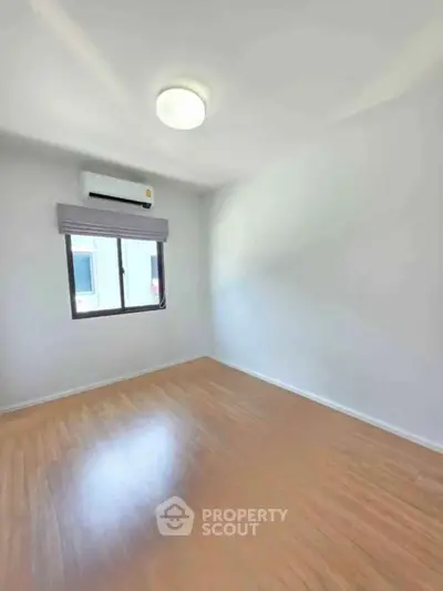 Bright empty room with wooden flooring and air conditioning, perfect for customization.