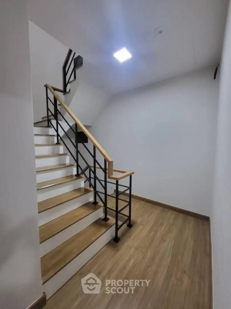 Modern staircase with sleek metal railing and wooden steps in a minimalist interior setting.