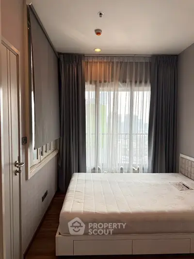 Cozy bedroom with large window and modern decor in high-rise apartment.