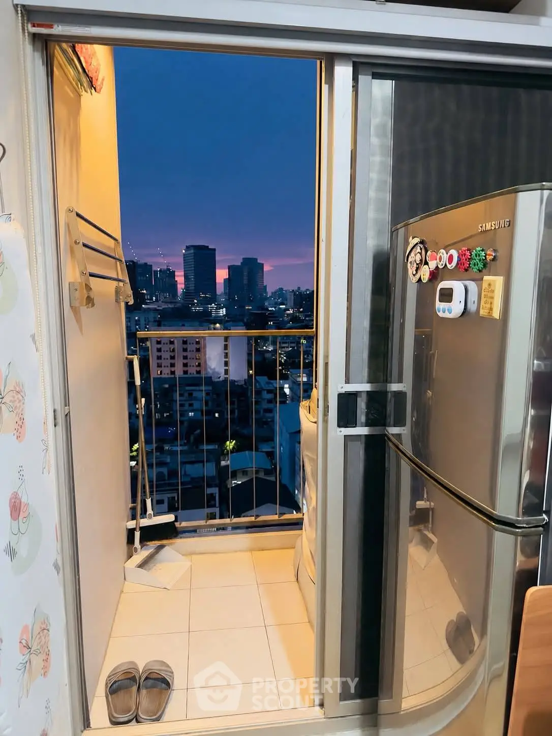 Charming urban balcony with city skyline view and modern fridge, perfect for cozy evenings.