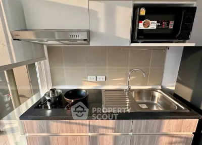 Modern kitchen with sleek design featuring stovetop, sink, and microwave in compact layout.