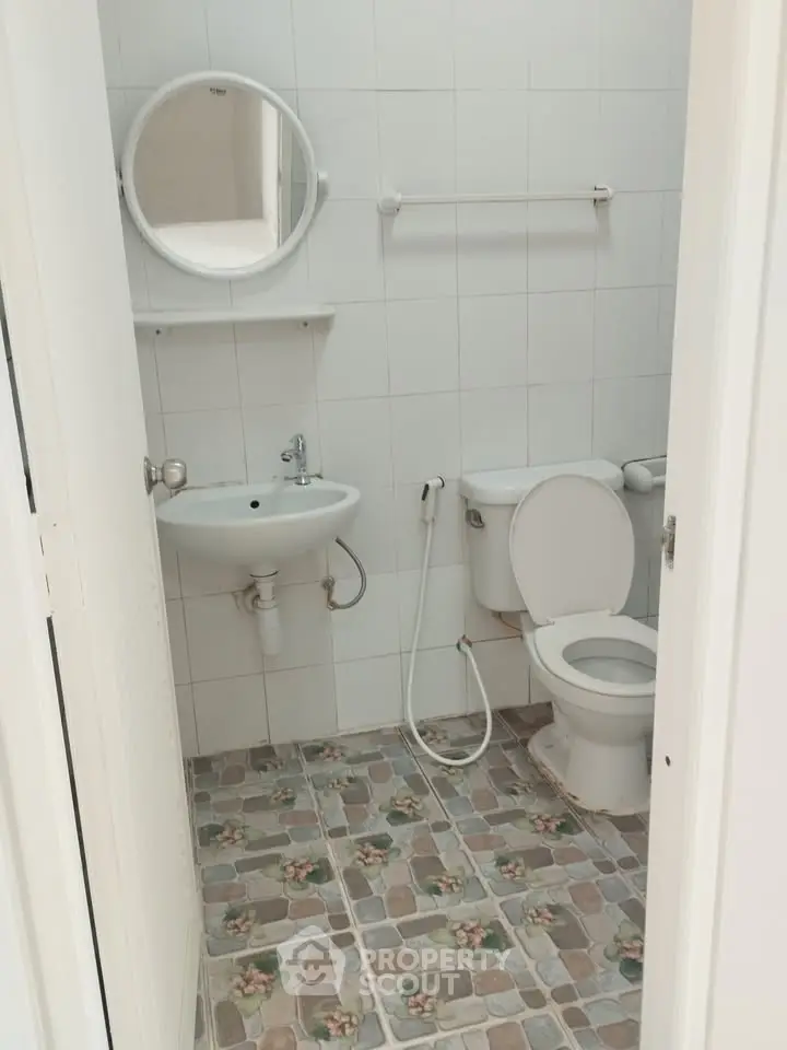 Compact bathroom with tiled floor and round mirror above sink.