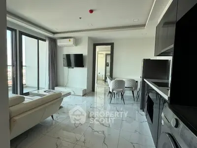 Modern living room with open kitchen and balcony view, featuring sleek furniture and marble flooring.