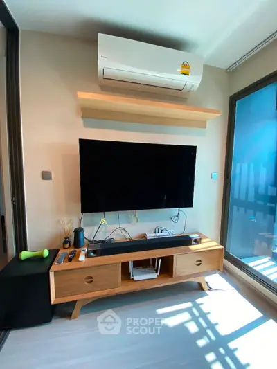 Modern living room with wall-mounted TV and air conditioner, stylish wooden furniture, and natural light.