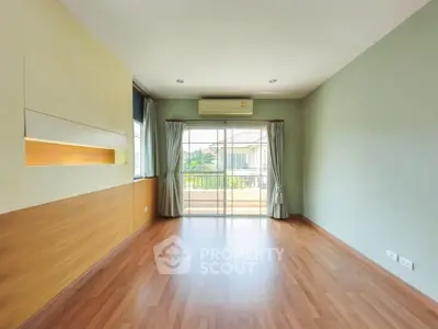 Spacious empty room with wooden flooring and balcony view, perfect for customization.