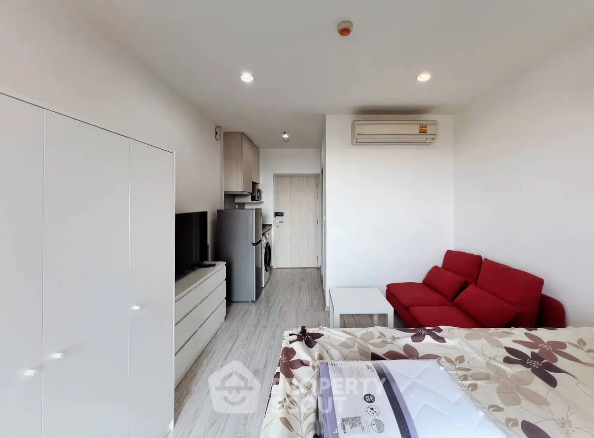 Modern studio apartment with red sofa, sleek kitchen, and bright ambiance.