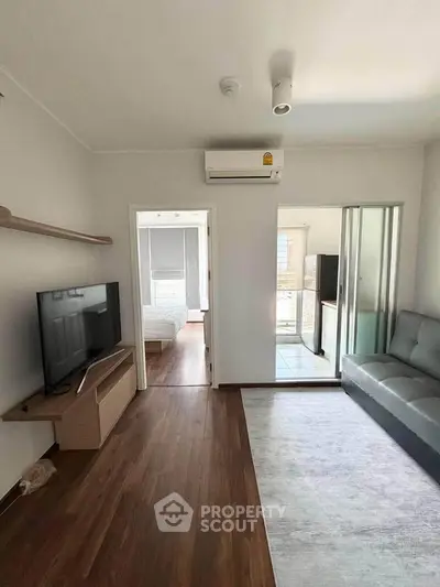 Modern living room with sleek furniture and air conditioning, leading to a bright bedroom and kitchen.