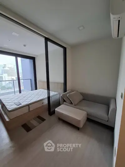 Modern bedroom with balcony view and cozy seating area in urban apartment.