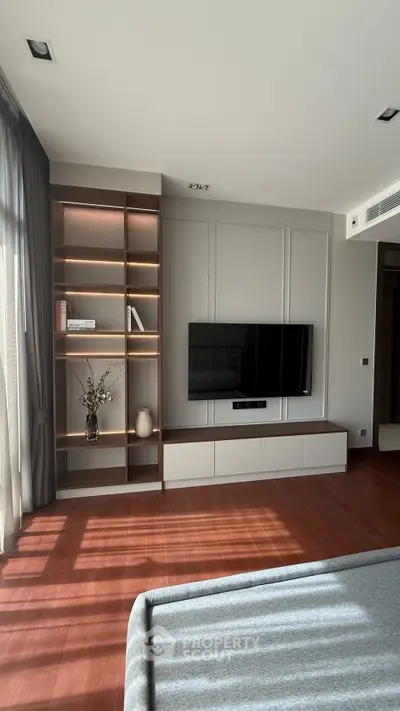 Modern living room with built-in shelves and wall-mounted TV, featuring elegant wood flooring.