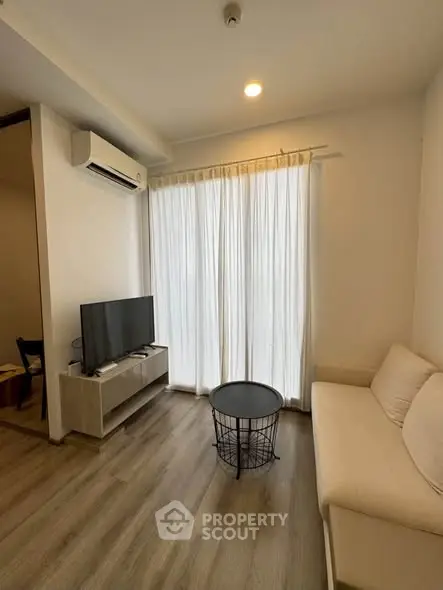 Modern living room with natural light, featuring a cozy sofa, TV, and elegant wooden flooring.