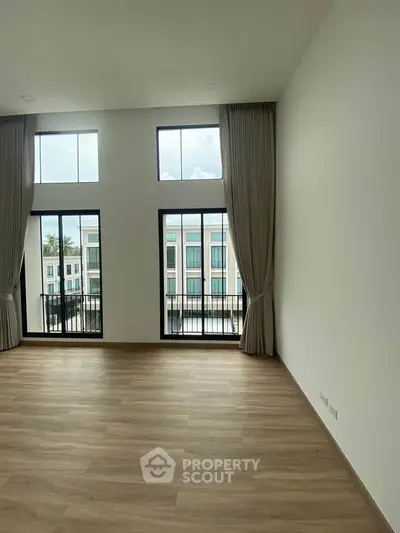 Spacious modern living room with high ceilings and large windows offering natural light and city views.