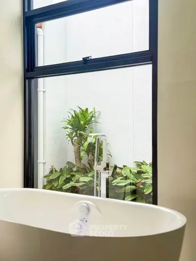 Luxurious bathroom with modern bathtub and large window overlooking lush greenery.